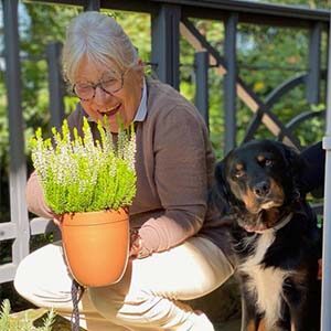 Woman on balcony holding a terracotta flower pot with a beautiful plant. Her dog is faithfully by her side